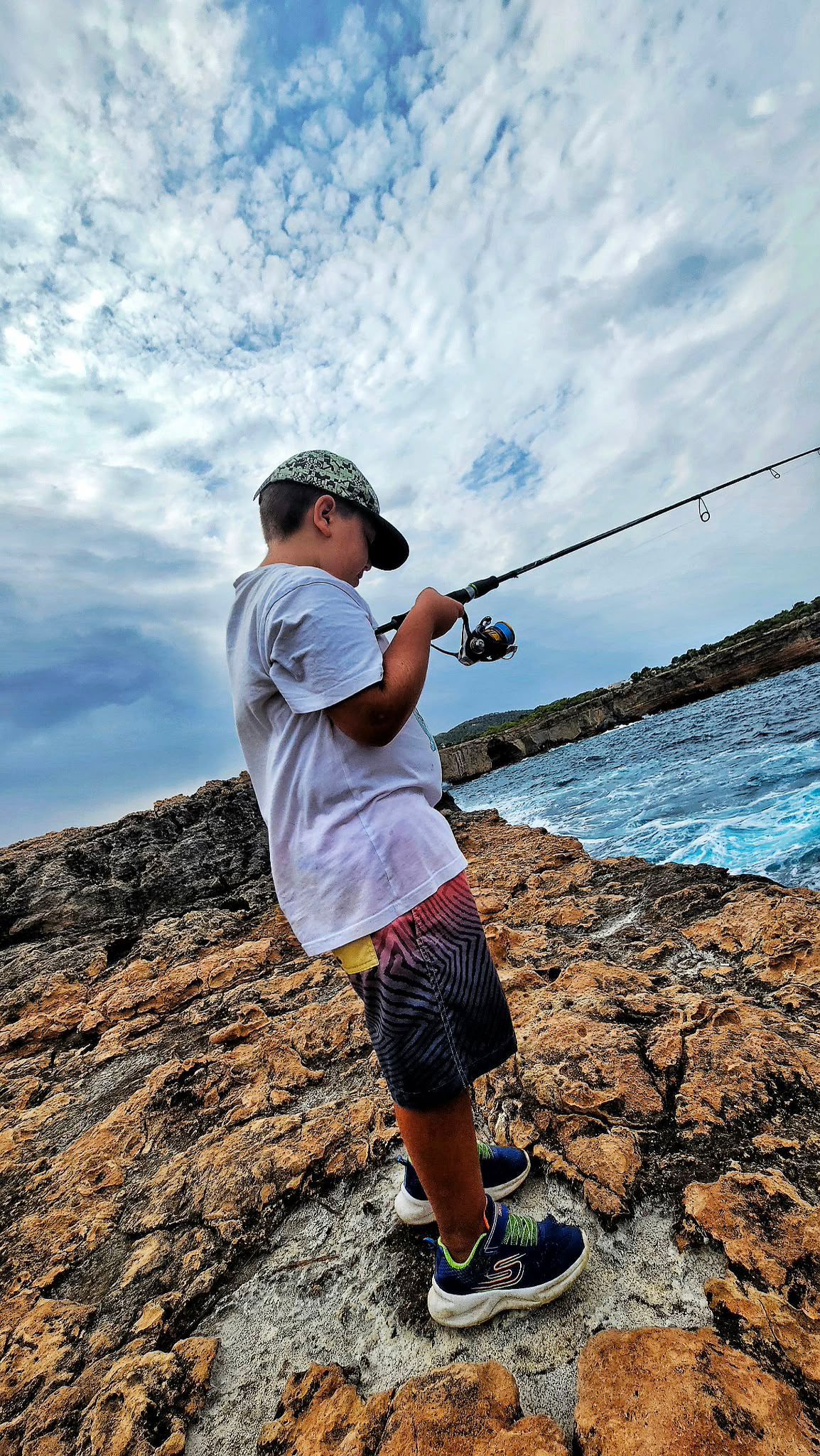 Pescador trabajando el jig con la caña alta sobre las rocas, técnica de jigging desde tierra
