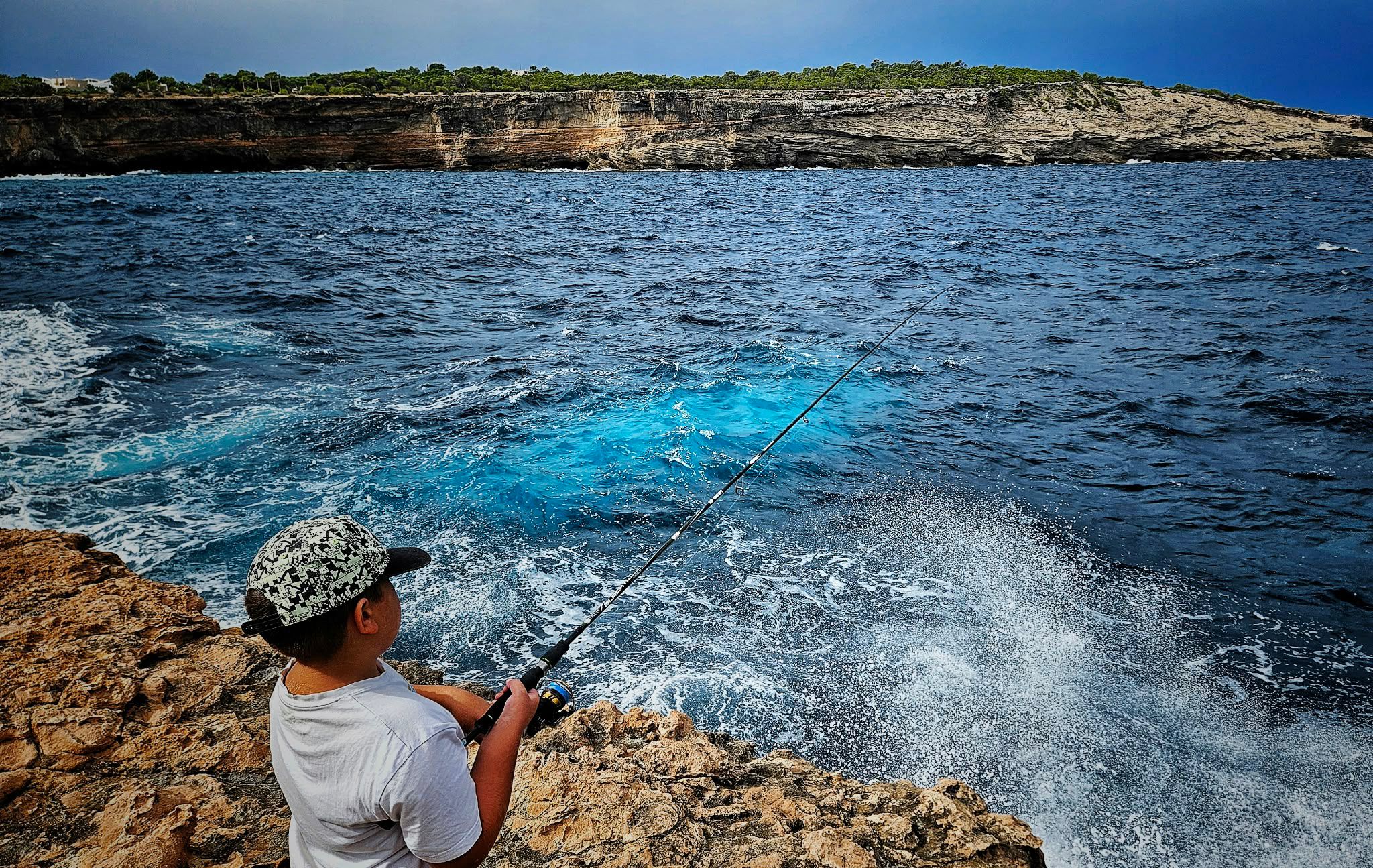 Joven pescando a jigging desde las rocas frente a un acantilado, buscando serviolas