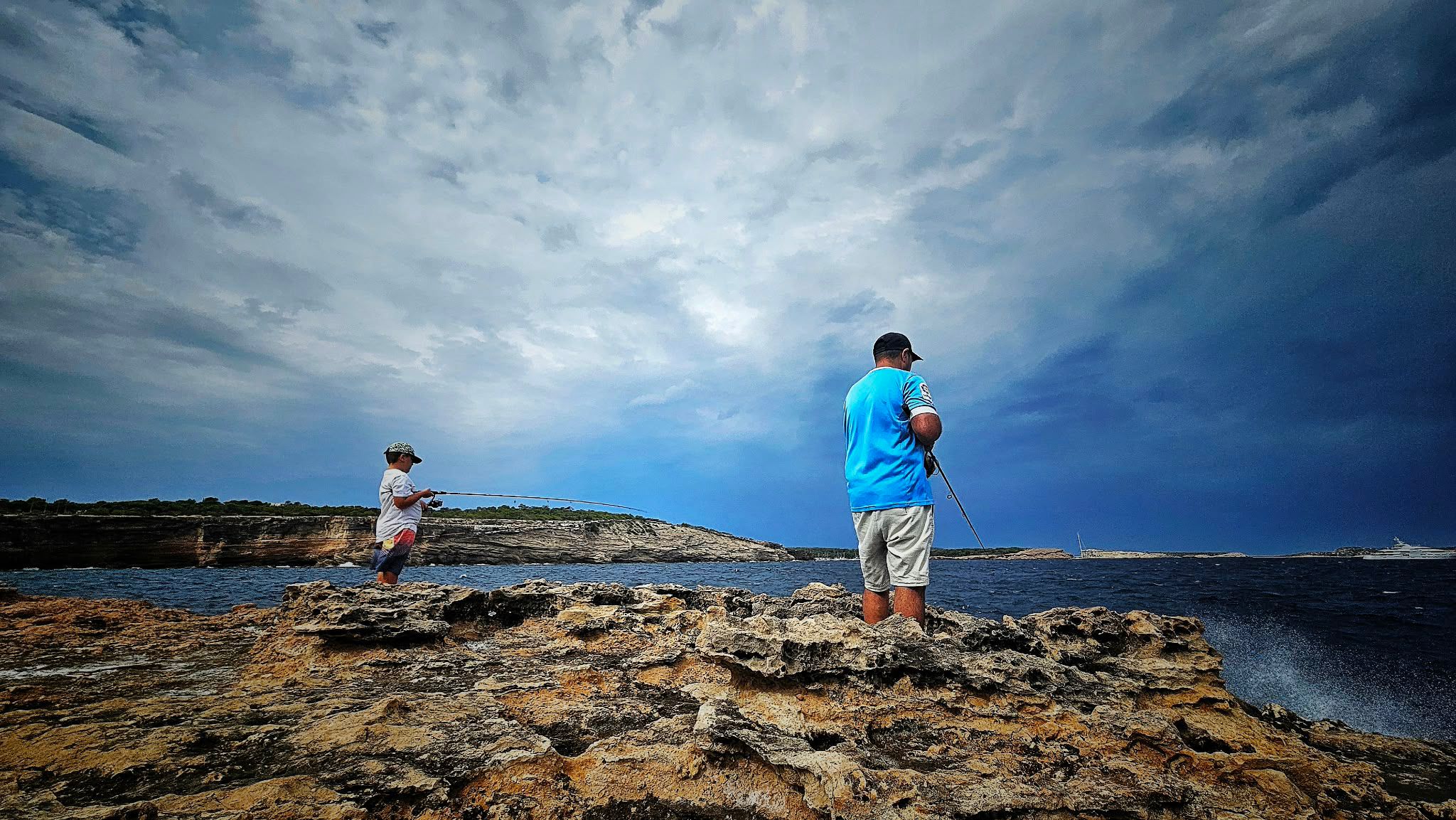 Padre e hijo pescando juntos a jigging desde las rocas al amanecer